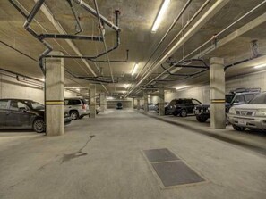 Un parking à plusieurs niveaux, avec des piliers en béton, un éclairage fluorescent et des voitures garées dans des emplacements prévus à cet effet.