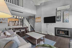 Un salon moderne doté d’une cheminée, d’un téléviseur à écran plat et d’un escalier menant à un niveau supérieur.