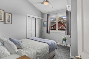 Ein Schlafzimmer mit einem Bett, einem Deckenventilator, einem Fenster mit Vorhängen, einer Tür und einer kleinen Pflanze.