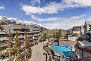 A resort with a swimming pool, multiple buildings, and snow-capped mountains in the background. - 2 bdrm penthouse with 180 Mountain view, heated pool & hot tubs (Canmore)