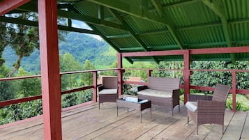 Un espacio de estar techado al aire libre con mobiliario de mimbre y vistas a un paisaje verde exuberante.