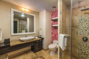 A modern bathroom with a granite countertop, a white sink, a large mirror, a toilet, and a shower with a pebble tile design. - Explore the Beautiful Stretch of the Beach! Pet-friendly, Beachfront, Pools! (Cabo San Lucas)