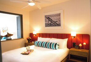 Ein Hotelzimmer mit einem Bett, einem Nachttisch, einer Wandlampe, einem gerahmten Bild und einem Deckenventilator.