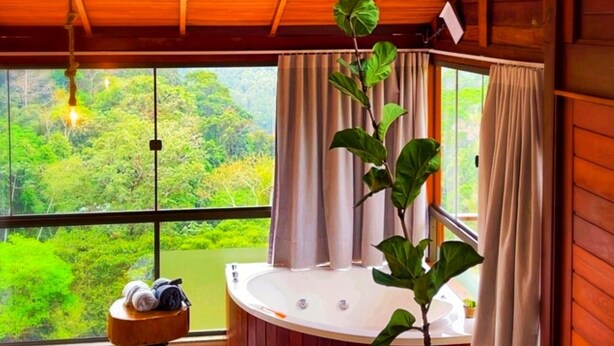 A wooden room with a hot tub, a small table with towels, and a view of a lush landscape.