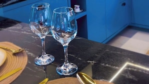 A kitchen with blue cabinets, a black countertop, and two wine glasses on a table.