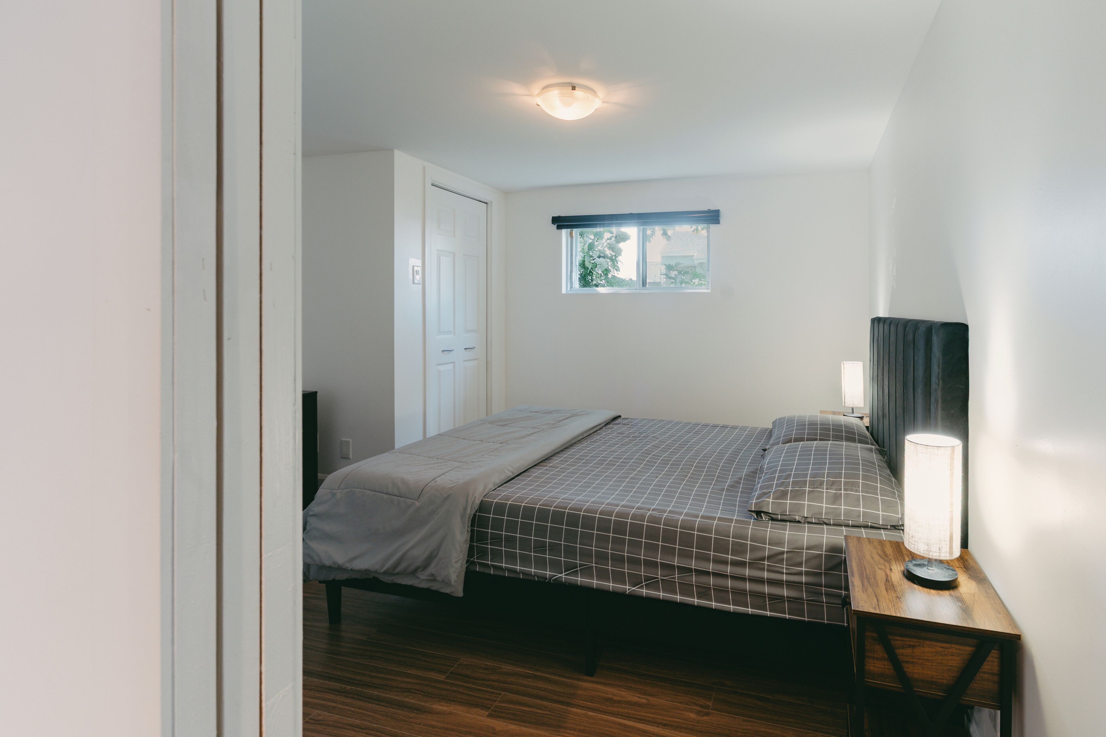 Un dormitorio con cama, mesita de noche, lámpara, ventana y puerta.
