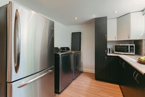 Une cuisine moderne dotée d’appareils électroménagers en acier inoxydable, de meubles de rangement aux couleurs sombres et d’un plancher en bois.