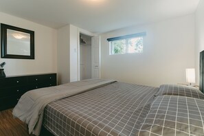 Une chambre à coucher avec un lit, une commode, un miroir, une fenêtre et une porte.
