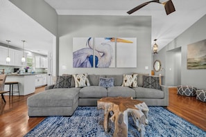 Ein modernes Wohnzimmer mit einem grauen Ecksofa, einem Holztisch und einem blauen Teppich mit Muster.