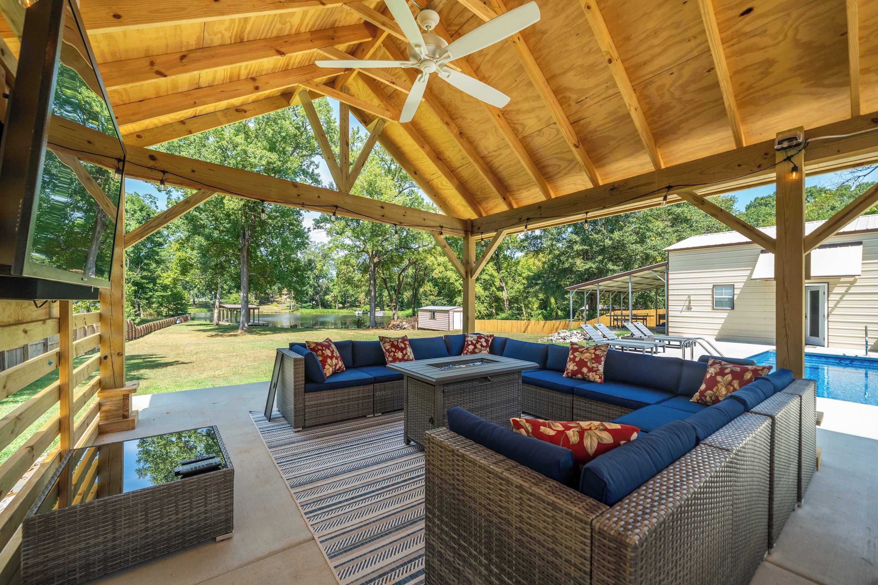 An outdoor covered patio with wicker furniture, a ceiling fan, and a view of a swimming pool and house.