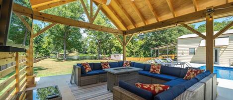 An outdoor covered patio with wicker furniture, a ceiling fan, and a view of a swimming pool and house.