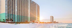 Un hôtel en bord de mer, avec plusieurs étages, une plage au premier plan et une vue sur les toits de la ville en arrière-plan.