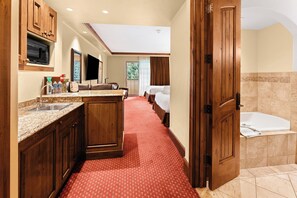 Quarto de hotel com cozinha compacta, uma cama grande, banheiro com banheira e vista para o exterior.