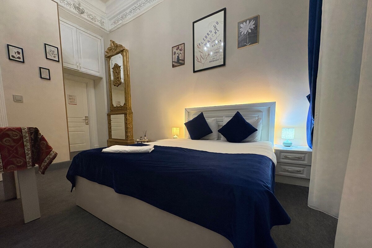 Una habitación de hotel con cama, mesita de noche, espejo y cuadros en las paredes.