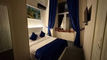 A bedroom with a bed, a painting, a window with curtains, and a wall-mounted TV.