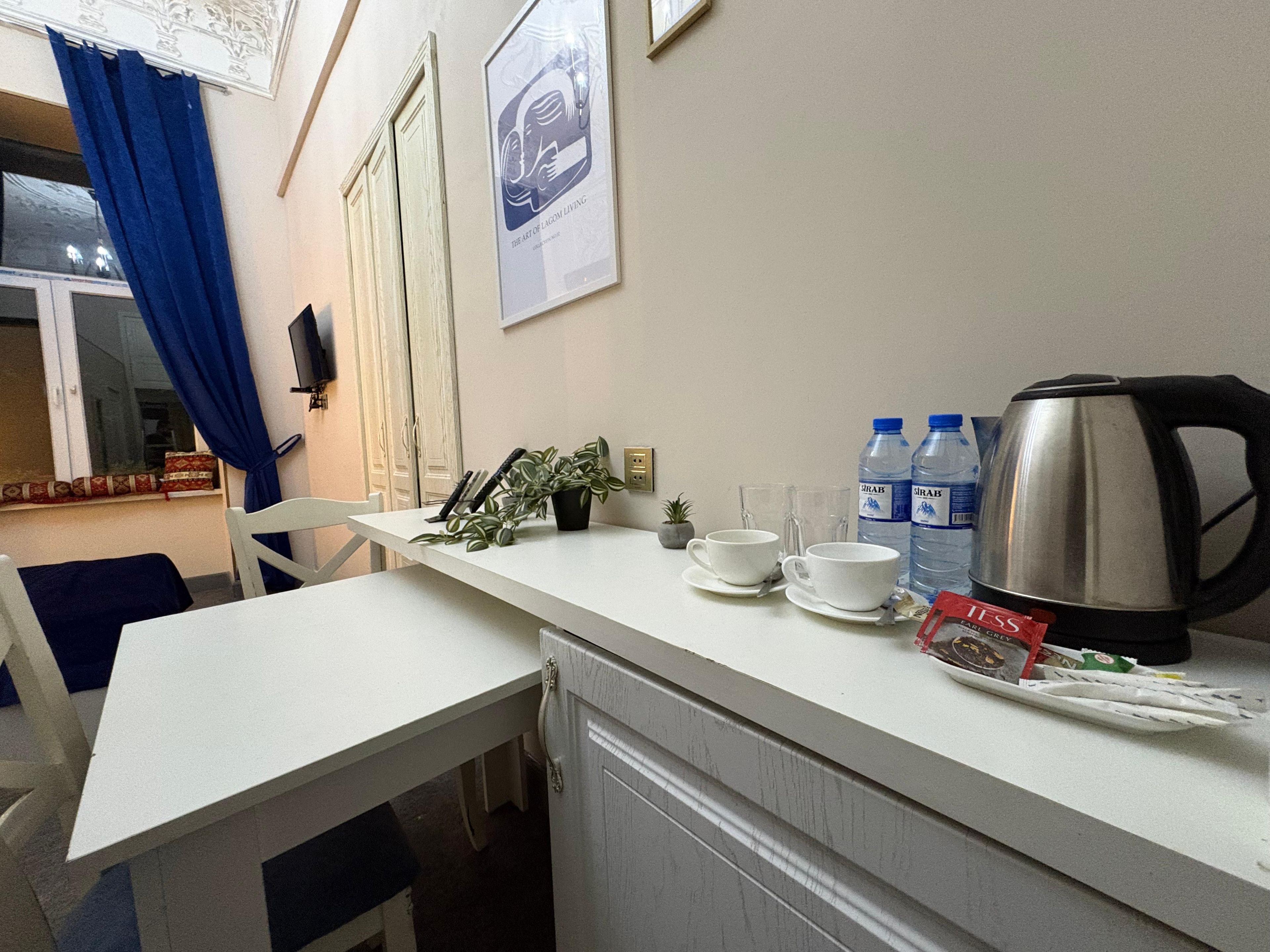 A kitchenette with a white countertop, a kettle, two water bottles, and a small potted plant.