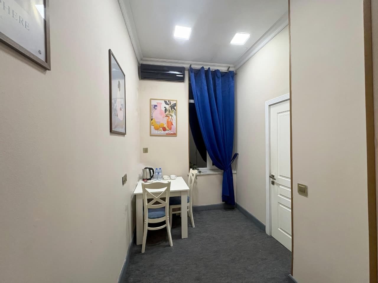 A small room with a table and chairs, a window with blue curtains, and a door.