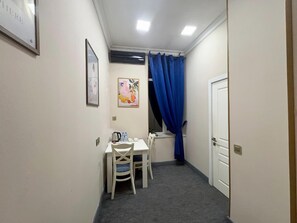 Una habitación pequeña con una mesa y sillas, un ventanal con cortinas azules y una puerta.