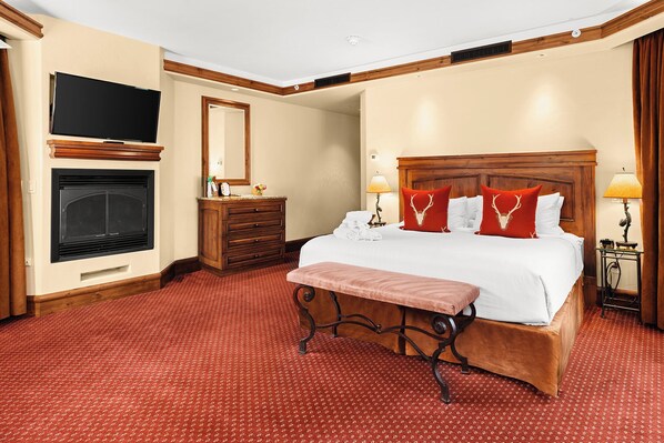 Quarto de hotel com uma cama grande, televisão, lareira e cabeceira de madeira.