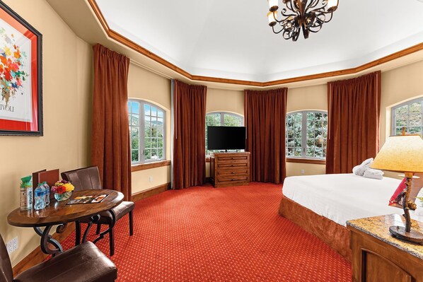 Ein Hotelzimmer mit einem großen Bett, einem Fernseher, einem Schreibtisch mit Stuhl und zwei mit Vorhängen versehenen Fenstern.
