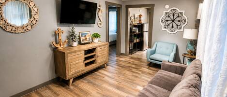 A living room with a wooden cabinet, a television, a blue armchair, and a sofa.
