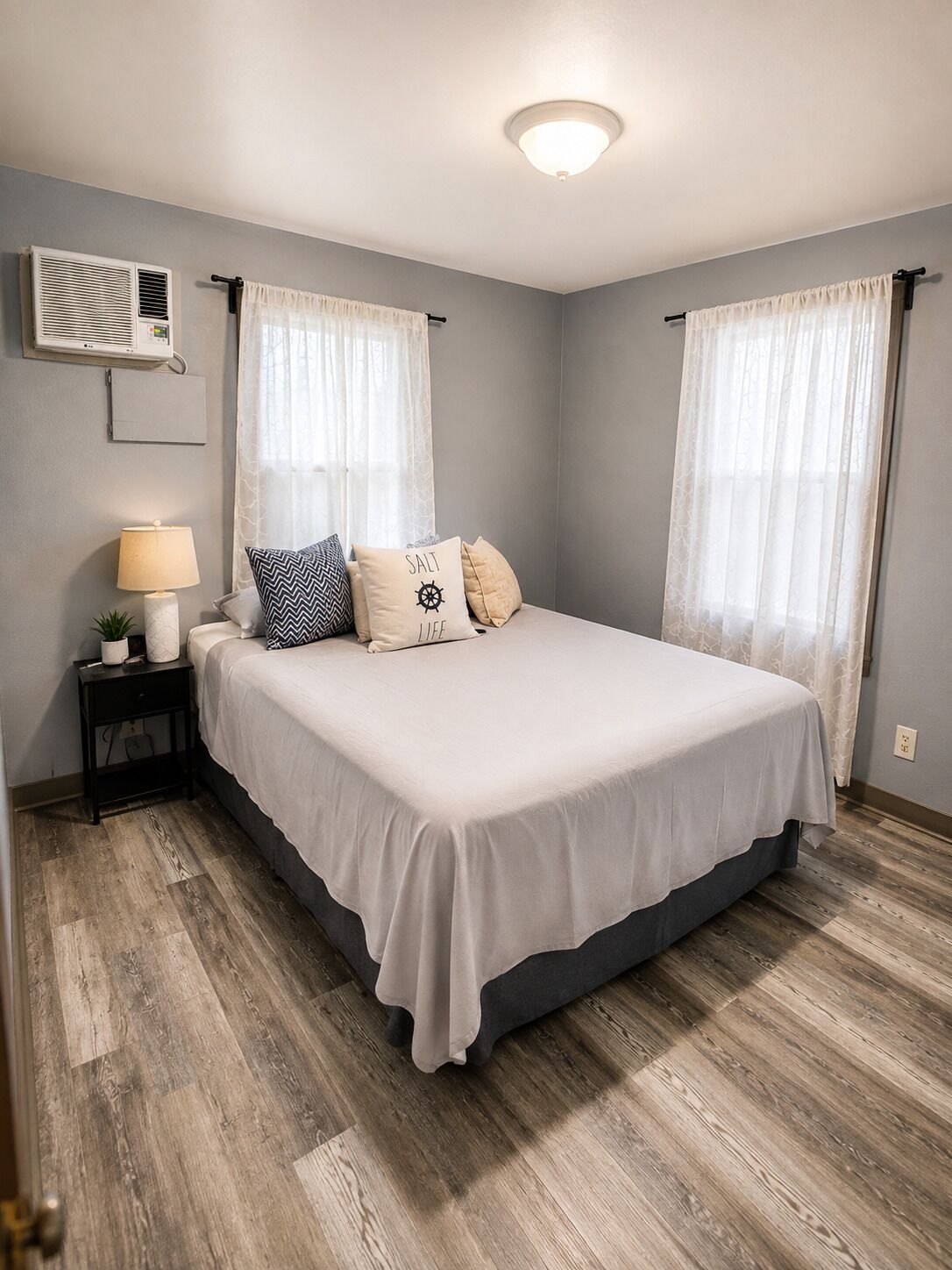 A bedroom with a bed, a nightstand, a lamp, and an air conditioning unit.