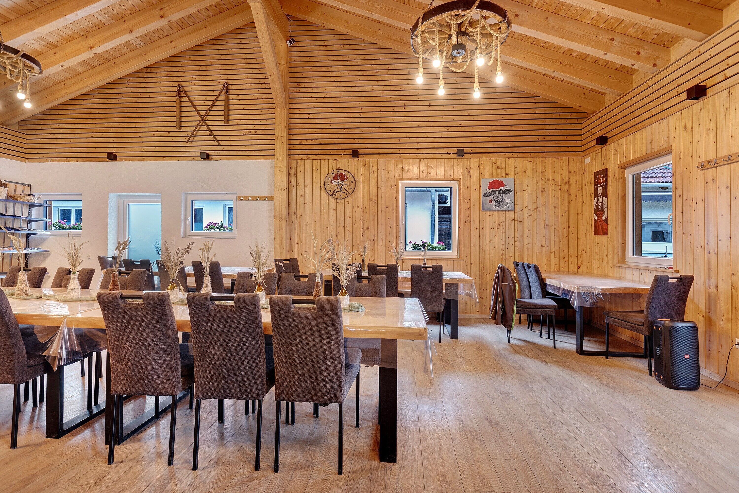 Un comedor amplio con mesas y sillas de madera, un candelabro y un reloj en la pared.