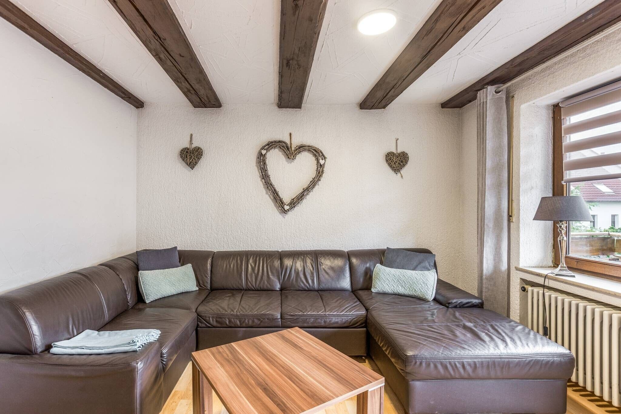 Een moderne woonkamer met een hoekbank, een houten salontafel en decoratieve hartdecoraties aan de muur.