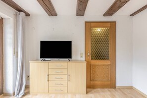 A room with a wooden cabinet, a television on top, a door with a glass panel, and a wooden ceiling.