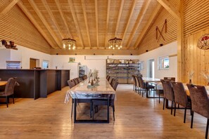 A spacious dining area with a long wooden table and chairs, a kitchen area with a refrigerator and stove, and a bookshelf filled with books. - Farmhouse Holiday Apartment with Heated Indoor Pool & BBQ Area for 6 Guests (Brigachtal)