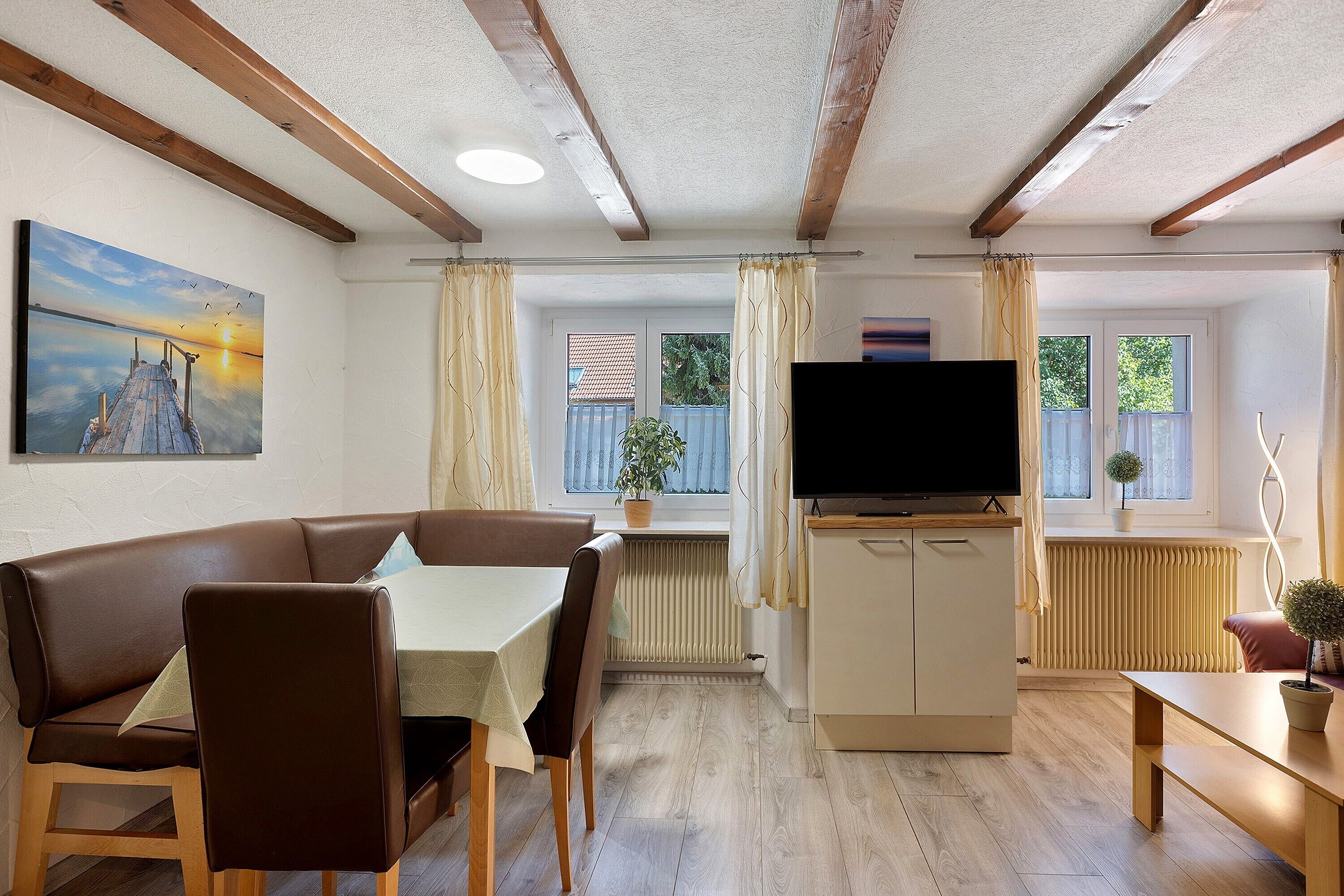Una sala de estar acogedora con un sofá de cuero marrón, una mesa de comedor, un televisor y una ventana con cortinas.