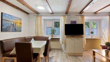 Una sala de estar acogedora con un sofá de cuero marrón, una mesa de comedor, un televisor y una ventana con cortinas.