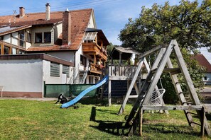 Zona residencial con una casa de techo de tejas rojas, balcón de madera y un tobogán azul en el jardín.