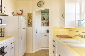 Eine Küche mit weißen Schränken, einem Kühlschrank, einer Uhr und einer gelben Arbeitsplatte.