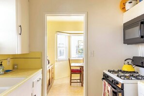 A compact kitchen with a gas stove, a microwave, and a window with blinds. - Wine Country Bungalow 2Bd/1Ba (Lompoc)