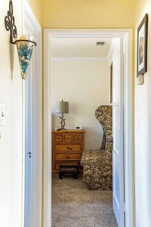 A narrow hallway with a wooden dresser and a floral armchair, leading to a room with a door. - Wine Country Bungalow 2Bd/1Ba (Lompoc)