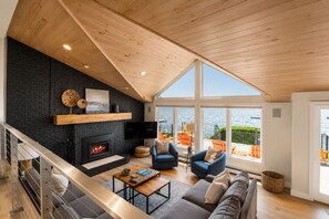 A modern living room with a fireplace, seating area, and large windows overlooking a body of water.