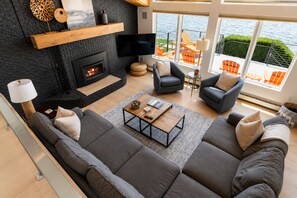 A modern living room with a fireplace, comfortable seating, and a view of the water.