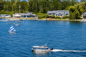 A lake with boats, a sailboat, and a speedboat. There are houses and trees in the background.