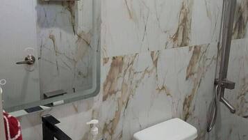 A bathroom with a marble wall, a white sink, a toilet, and a shower.