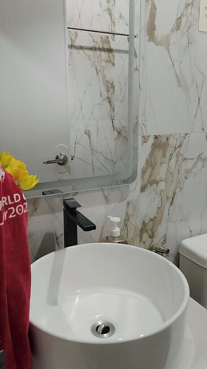 A bathroom with a white sink, a mirror, and a marble wall.