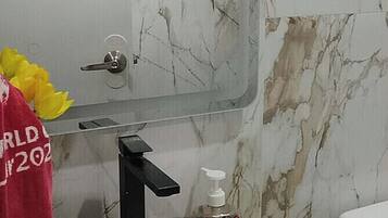 A bathroom with a white sink, a mirror, and a marble wall.