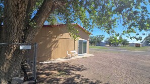 A small wooden shed with a red roof, a sliding glass door, and a white table and chair set outside.