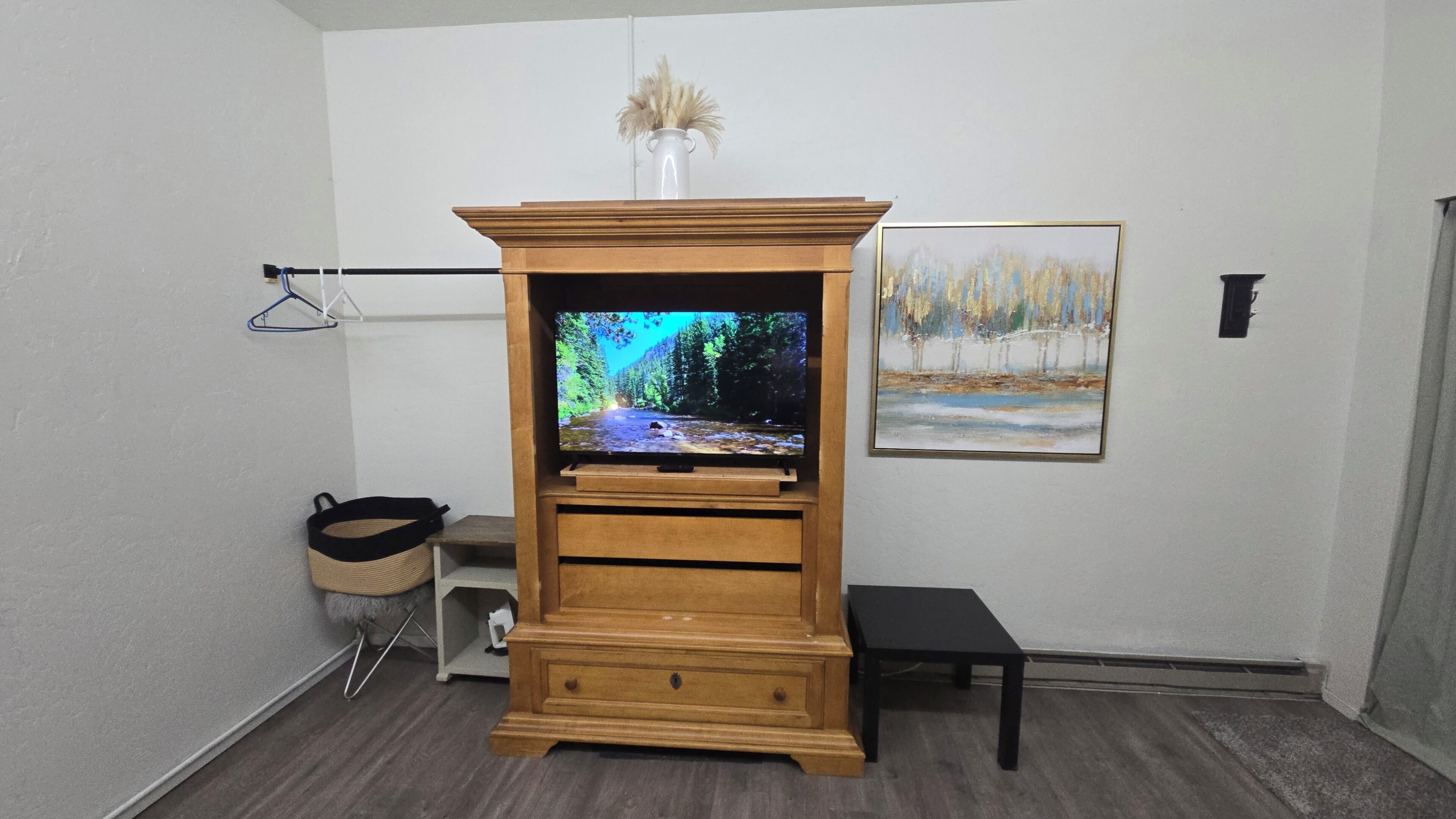 Une pièce comprenant un meuble de rangement en bois abritant un téléviseur, un petit banc et un tableau accroché au mur.