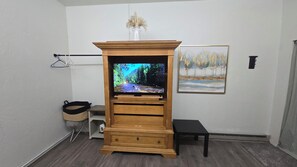 A room with a wooden entertainment center housing a television, a small bench, and a painting on the wall.