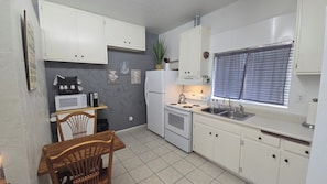 A compact kitchen with white cabinets, a microwave, a refrigerator, a stove, and a sink.