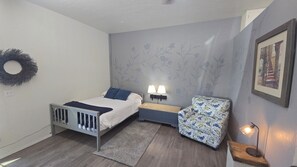 Een slaapkamer met een bed, bedlampen, een stoel, een klein tafeltje, een aan de muur hangend schilderij en een decoratieve krans.