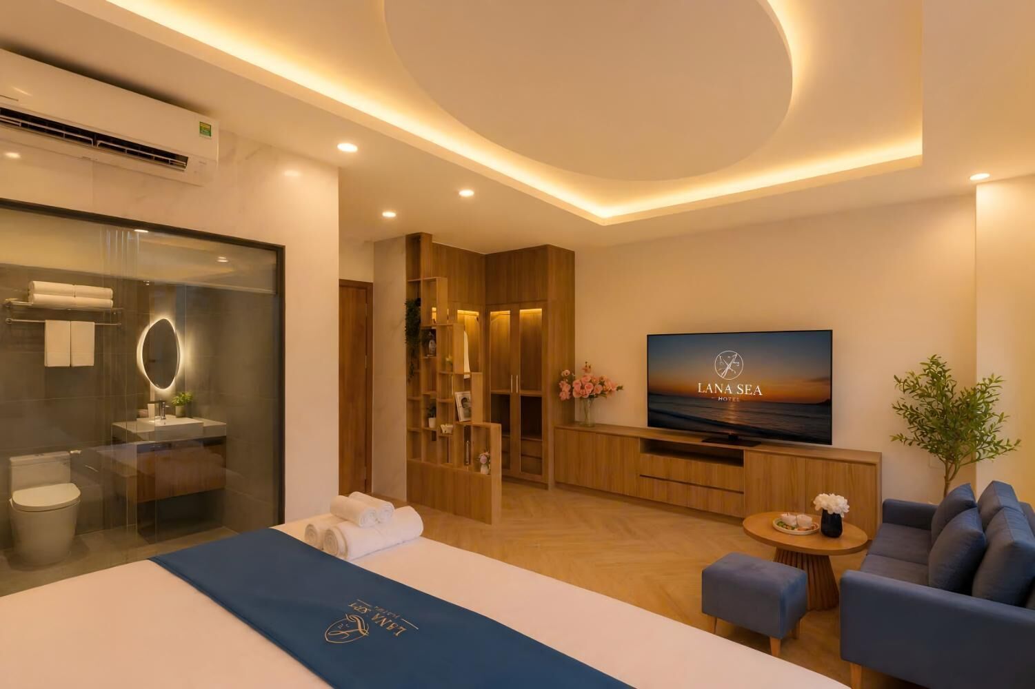 A modern hotel room with a bed, a TV, a seating area, and a bathroom.