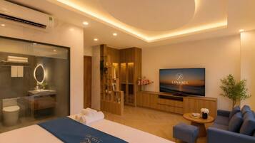 A modern hotel room with a bed, a TV, a seating area, and a bathroom.