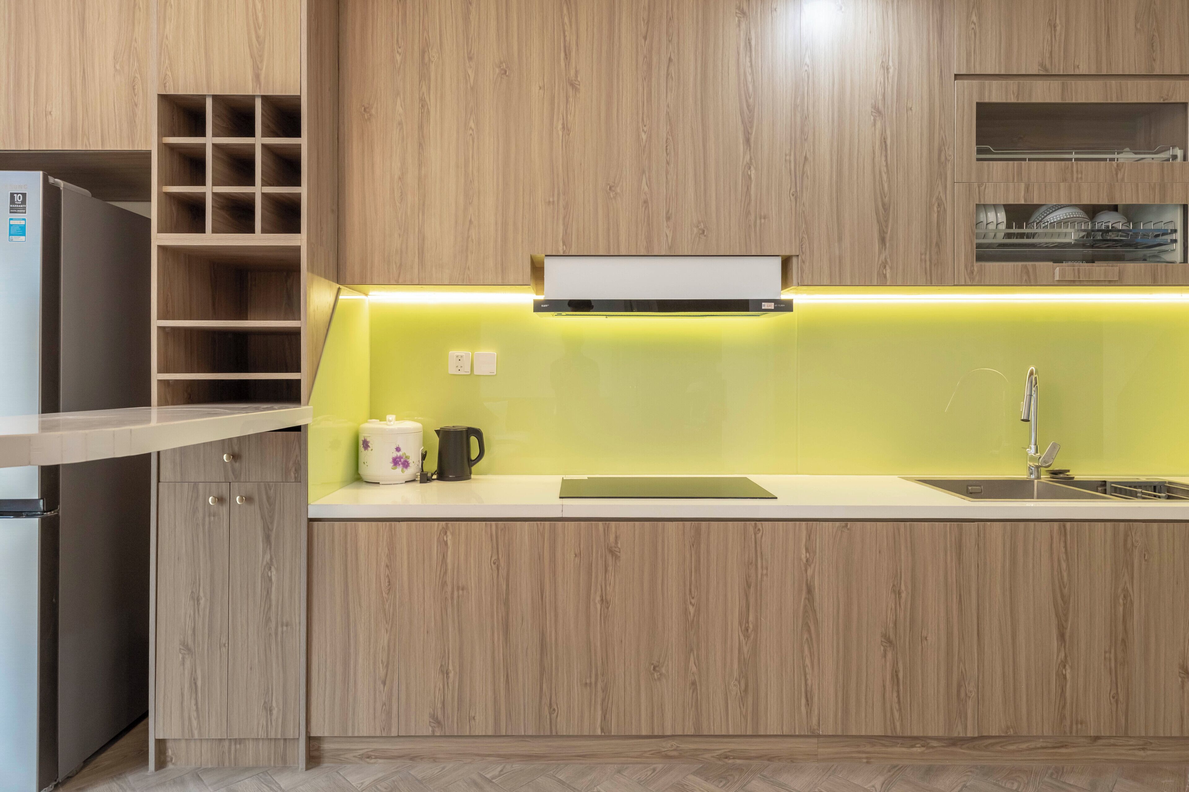 Una cocina moderna con armarios de madera, horno empotrado, lavaplatos y encimera con hervidor y cafetera.